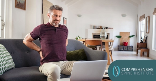 Man holding his lower back sitting on a couch.