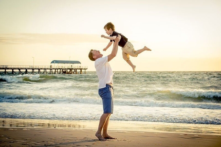 Father lifting son up into the air by the beach